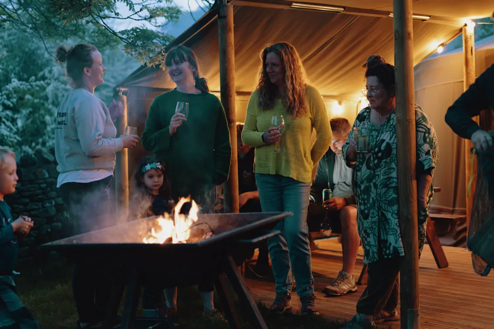 A group of women gather around a fire pit at Masons Campsite