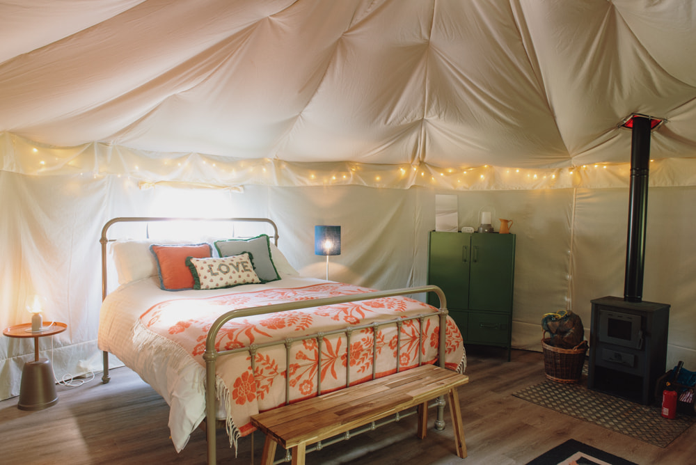 Inside a yurt - a large bed with cushions, a cupboard and a log burner